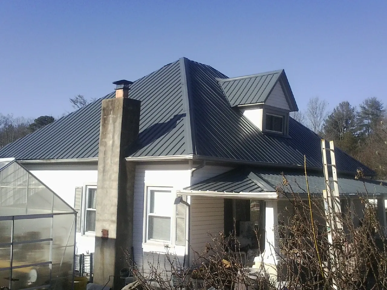 Dark blue standing seam metal roof on a white farmhouse with dormer — Slate & Tile Roof Repair by Roofing Brothers in Aplington