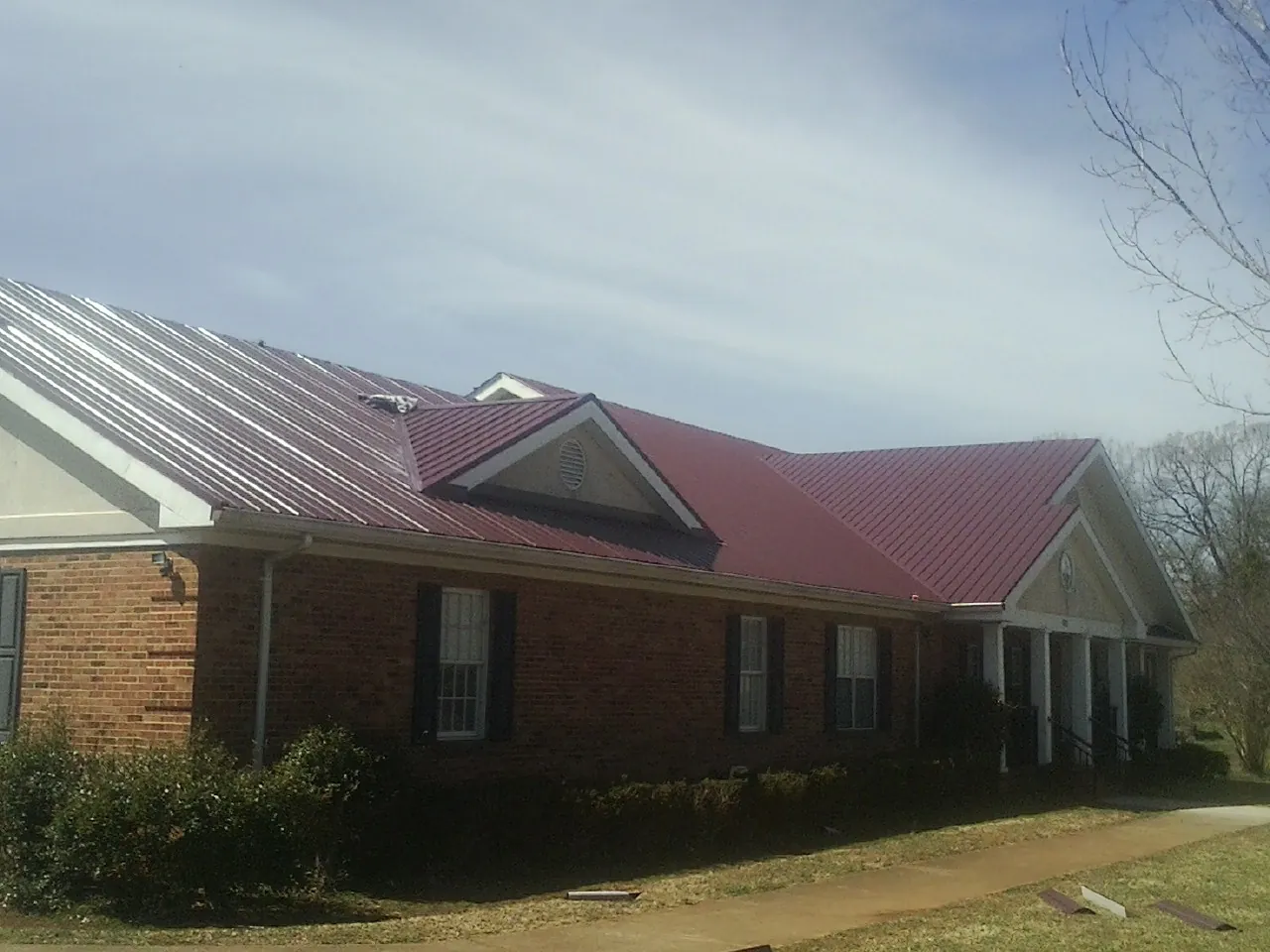 Red metal roof with gabled entries on a long brick building, from a Hail Damage Roof Repair job in Aplington