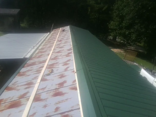 Old rusted panels beside newly installed green metal roofing — Wind Damage Roof Repair by Roofing Brothers in Aplington