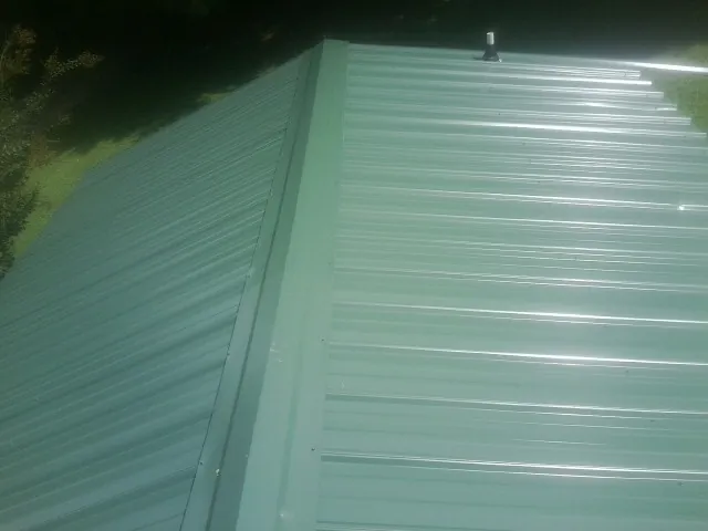 New green metal panels meeting at the ridge of a roof — Flat Roof Repair work by our crew in Aplington