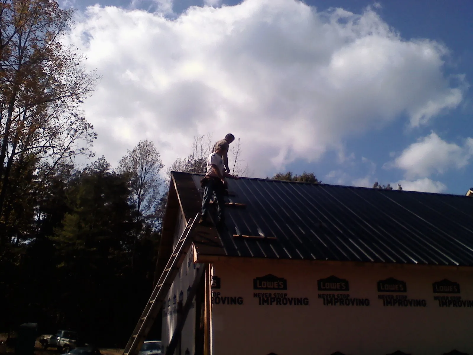 Roofer fastening dark metal panels high against a cloudy sky, from a Roof Inspection job in Aplington