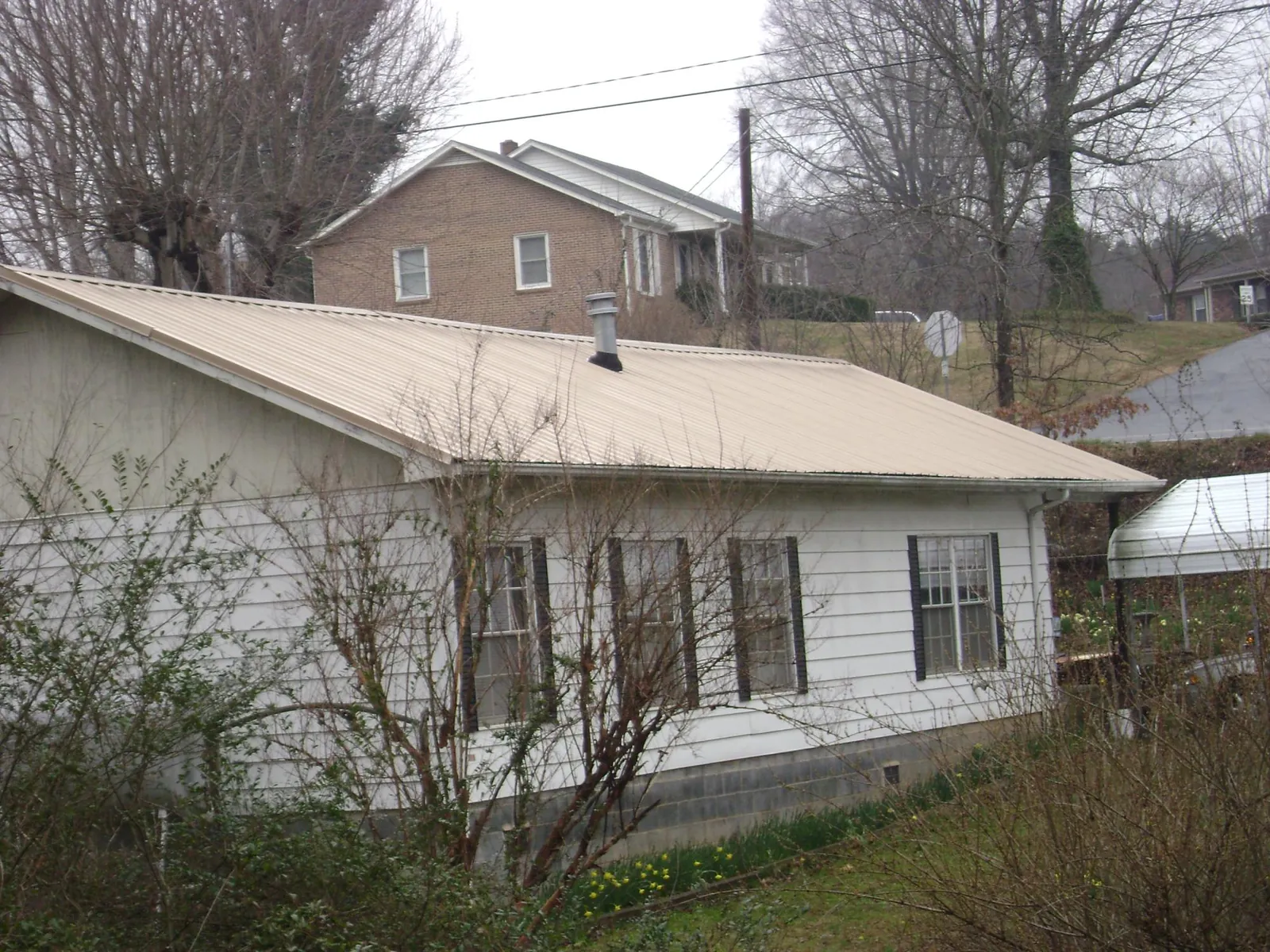 Tan metal roof on a white sided house set into a hillside — Commercial Roofing by Roofing Brothers in Aplington