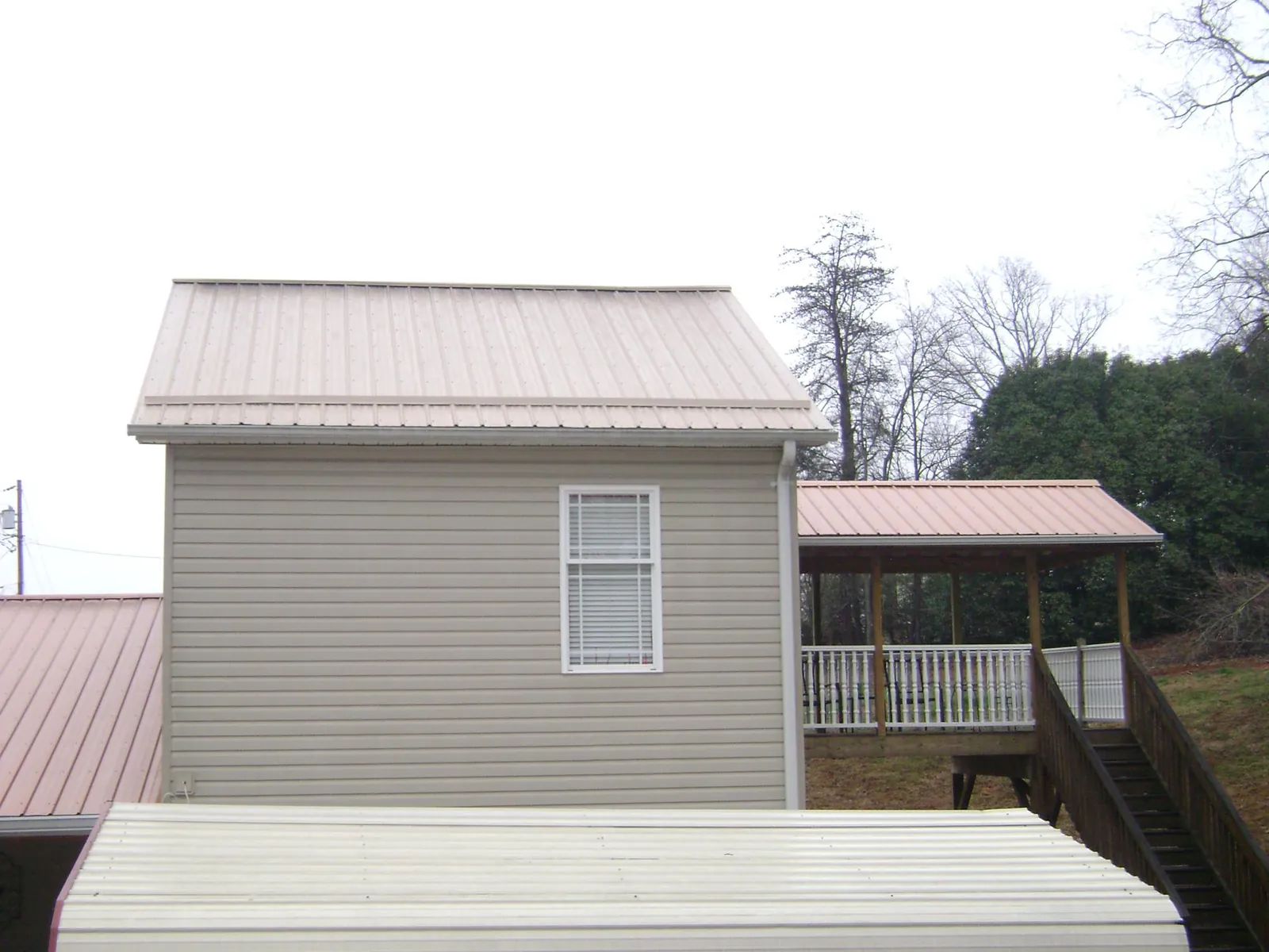 Tan metal roofs on a two story addition and attached porch, from a Roof Replacement job in Aplington