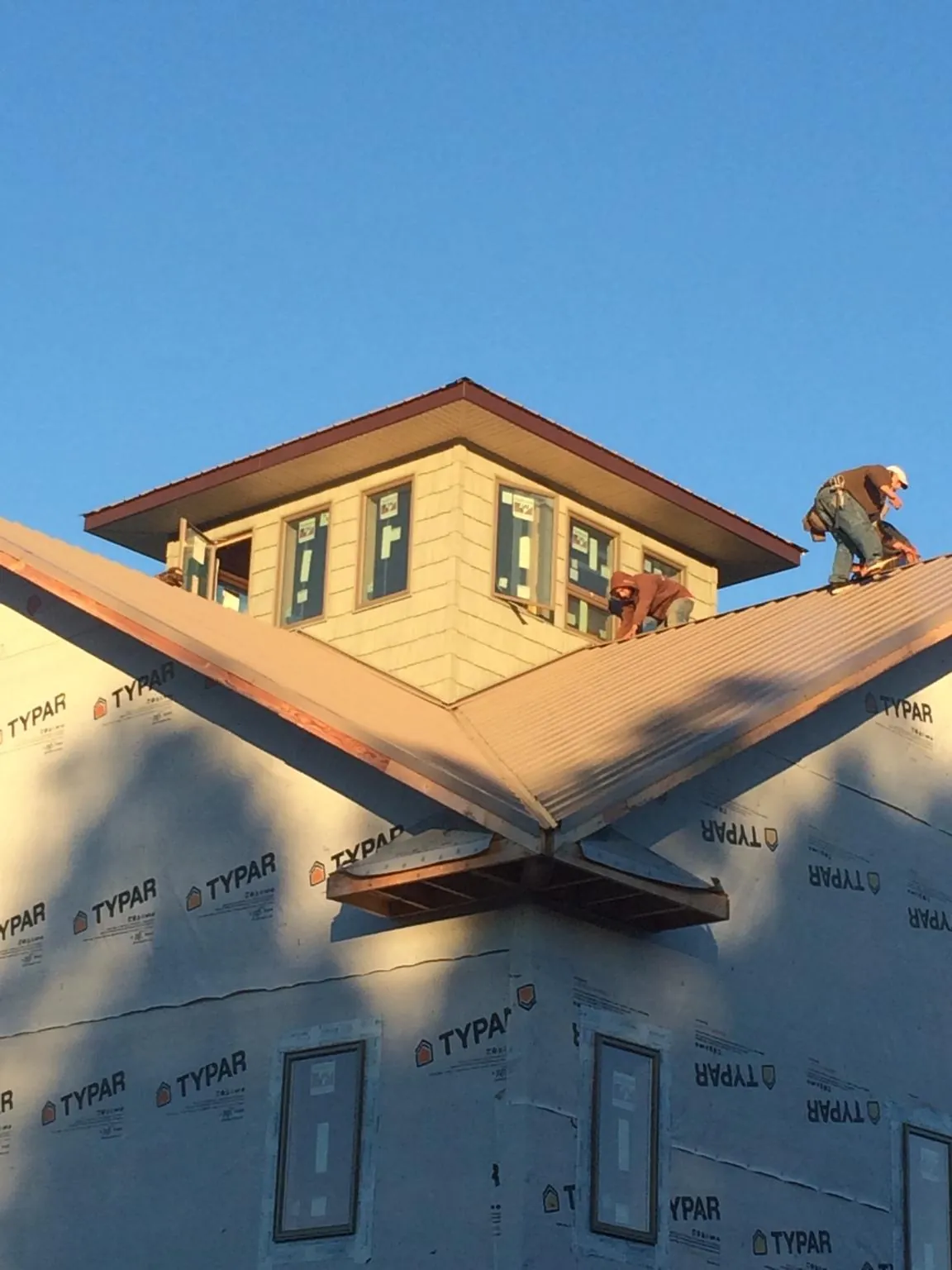 Roofers working around a rooftop cupola on a new metal roof at sunset — Roof Waterproofing in Aplington by Roofing Brothers
